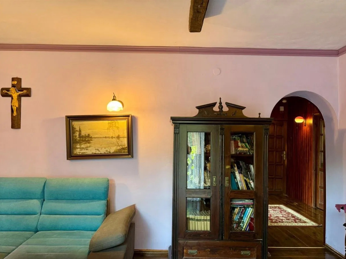 This inviting indoor space features a comfortable teal sectional sofa positioned against a soft pink wall, creating a warm and personalized ambiance. An antique-style wooden boo...