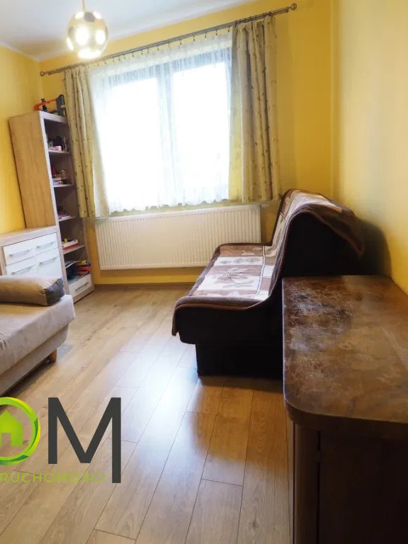 This cozy room features bright yellow walls that create a cheerful and inviting atmosphere, complemented by light wood laminate flooring throughout. A large window, dressed with...