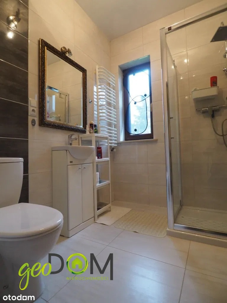 This is a clean and functional bathroom featuring a toilet, a vanity with storage, and a glass-enclosed shower. The walls are tiled with light-colored ceramic tiles, and the flo...