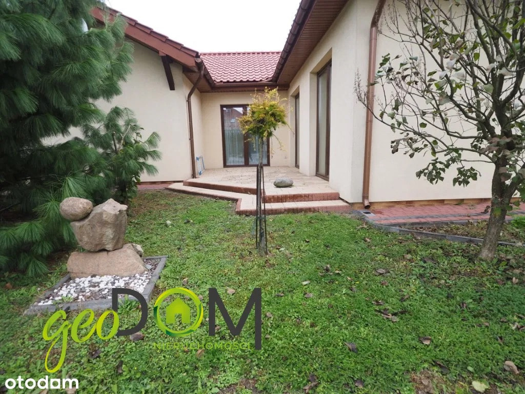 The exterior showcases a charming bungalow with a modern aesthetic, featuring light-colored stucco walls and a dark tiled roof. Large windows and glass doors offer glimpses into...