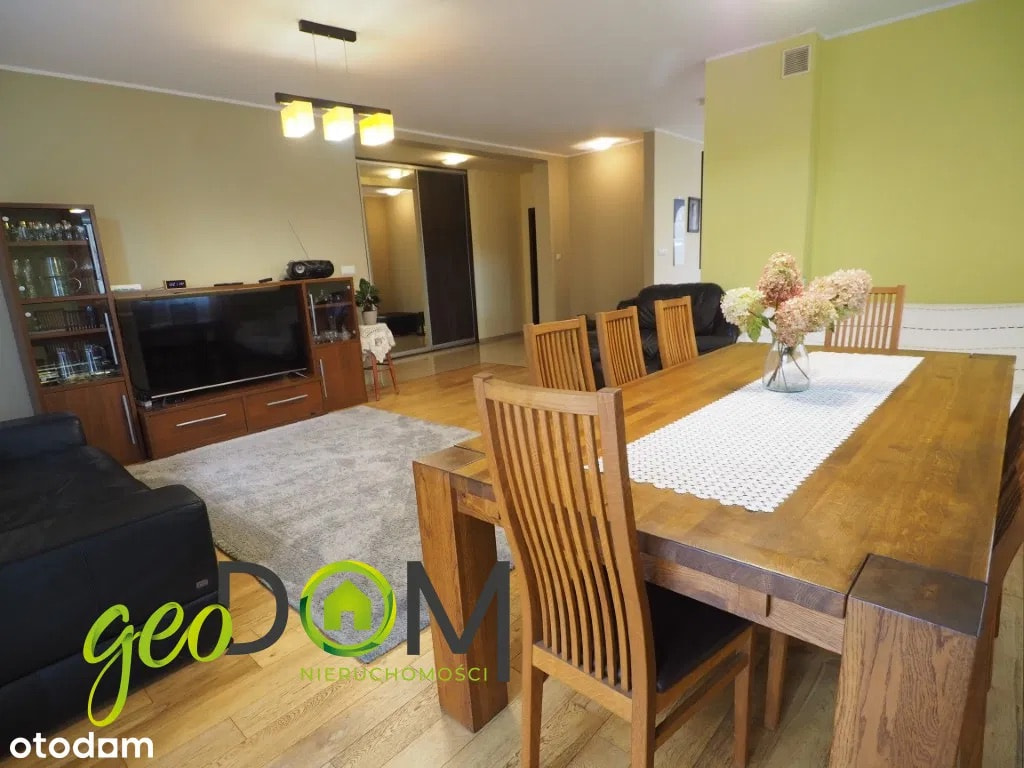 This open-concept living and dining area features warm wooden floors and a large dining table set for six. The dining space is illuminated by a modern pendant light fixture, whi...