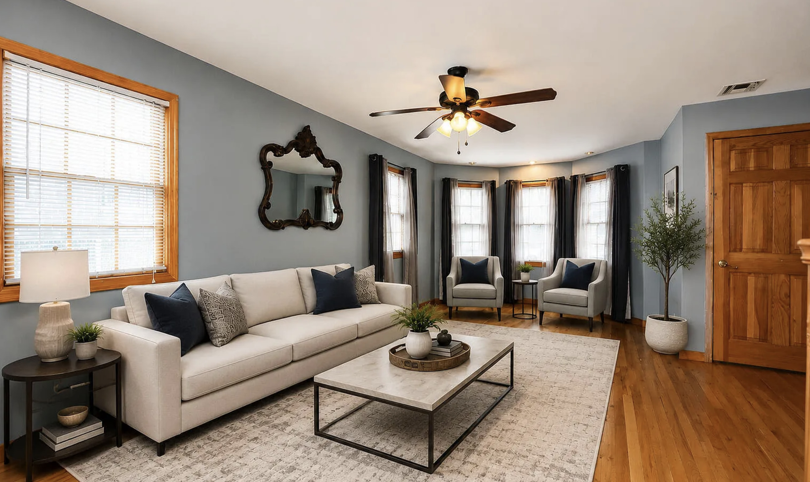 This inviting living room features a neutral color palette with a large, comfortable sectional sofa and two accent chairs. The space is illuminated by natural light streaming th...